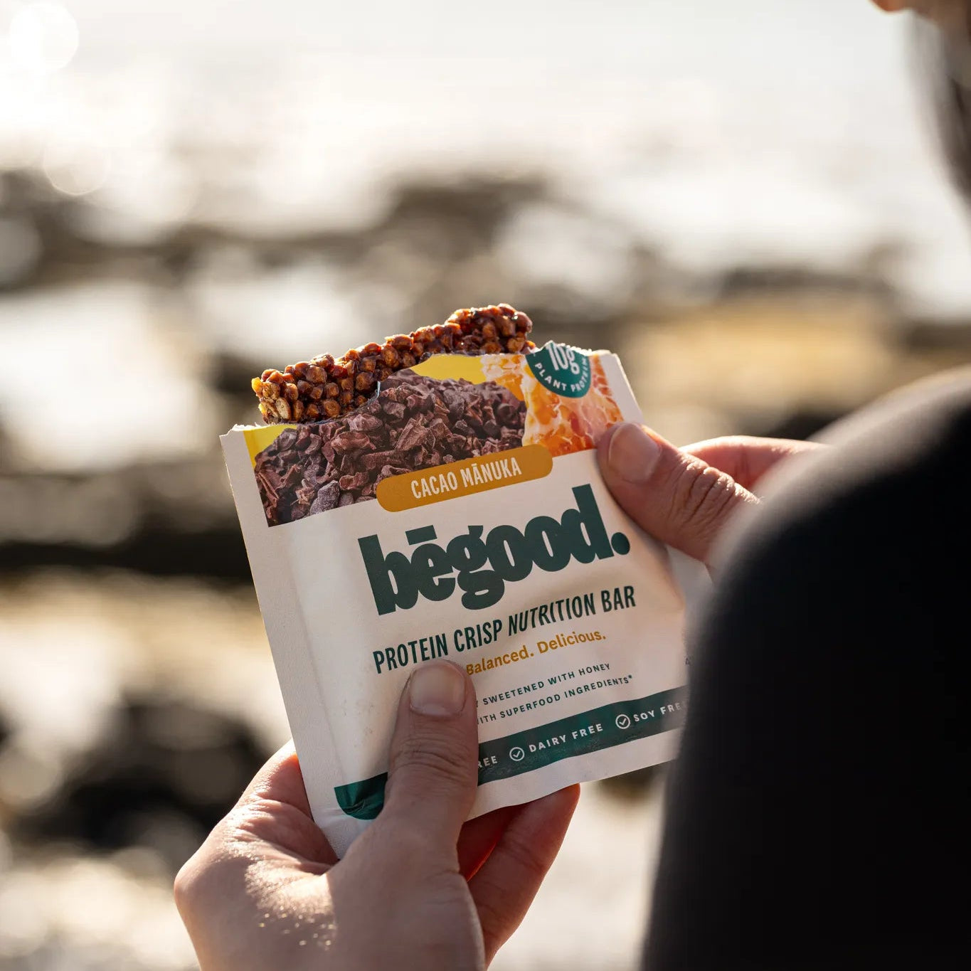 Person holding a 'begood' protein crisp nutrition bar package outdoors.