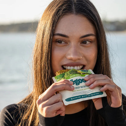 Woman holding a bēgood protein bar outdoors with water in the background