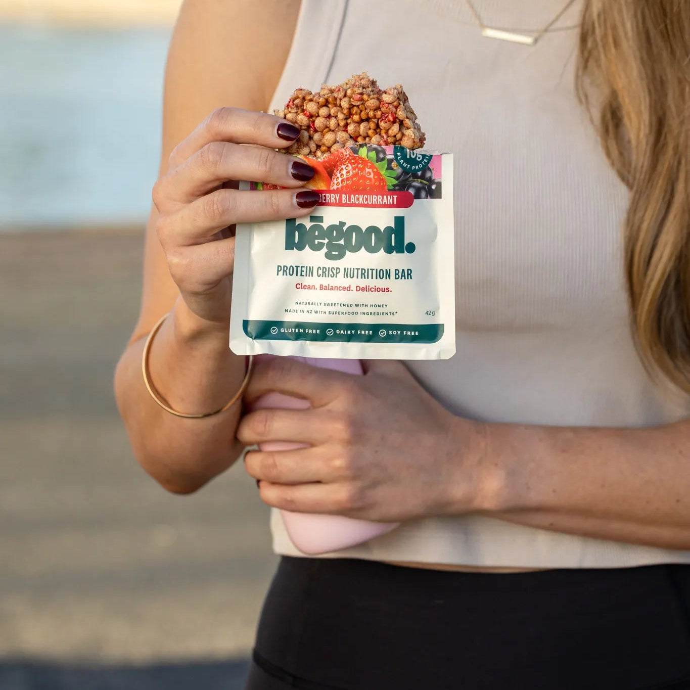 Person holding a 'begood' protein crisp bar package by a body of water.