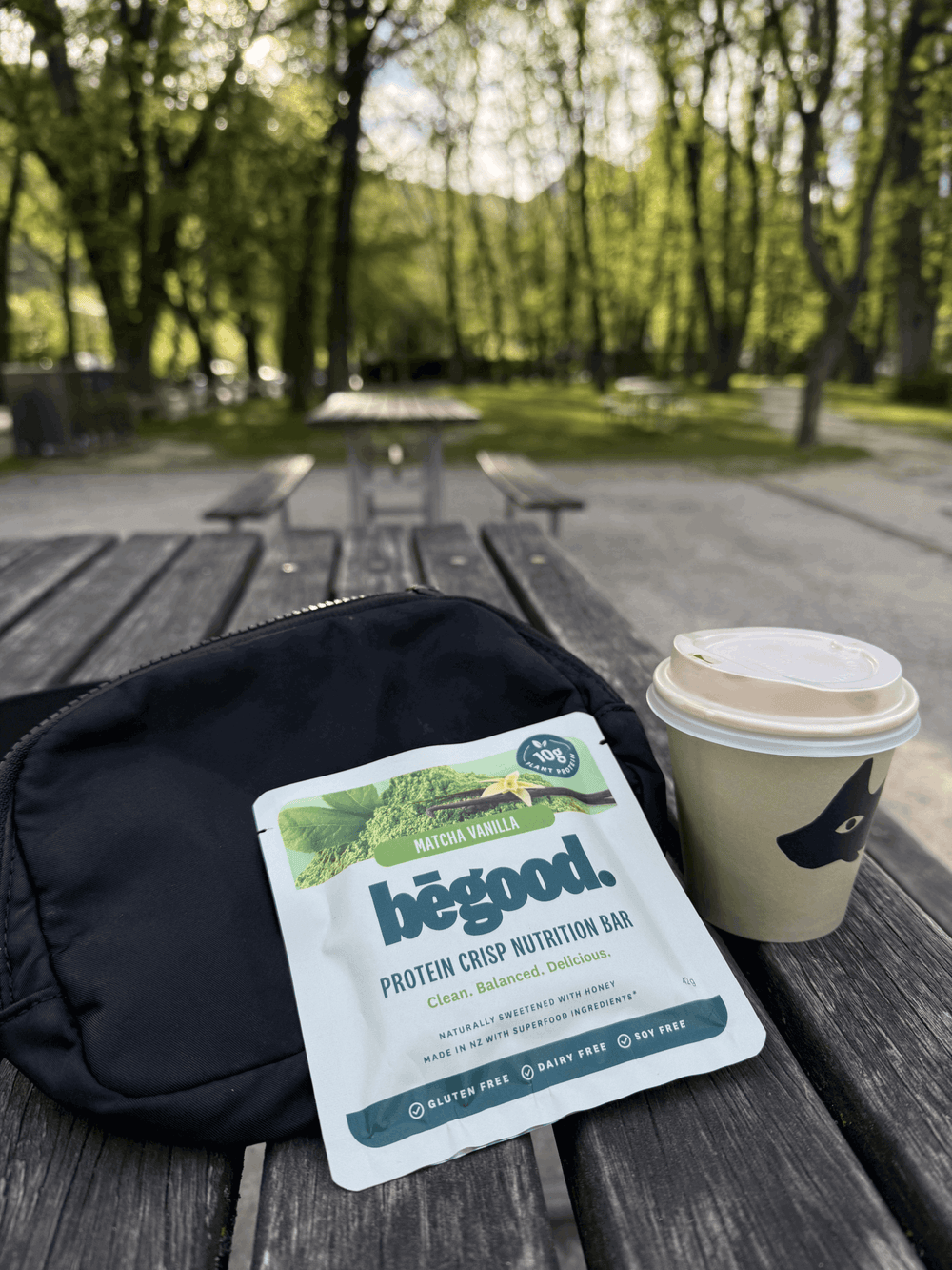 Protein crisp nutrition bar package and coffee cup on a wooden table outdoors.