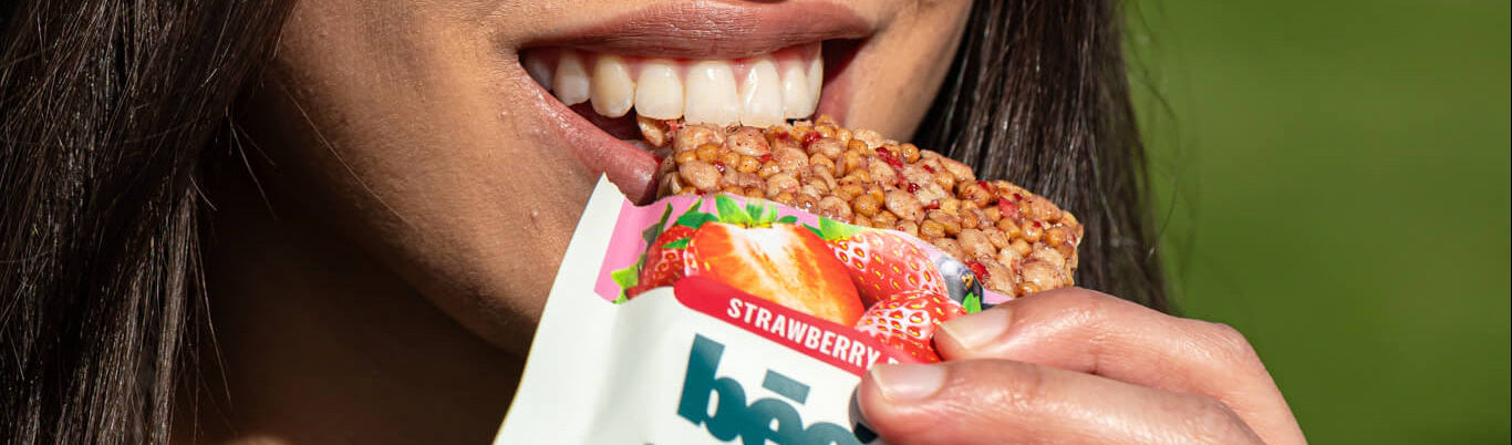 Person eating a strawberry-flavored begood nutrition bar with a blurred green background